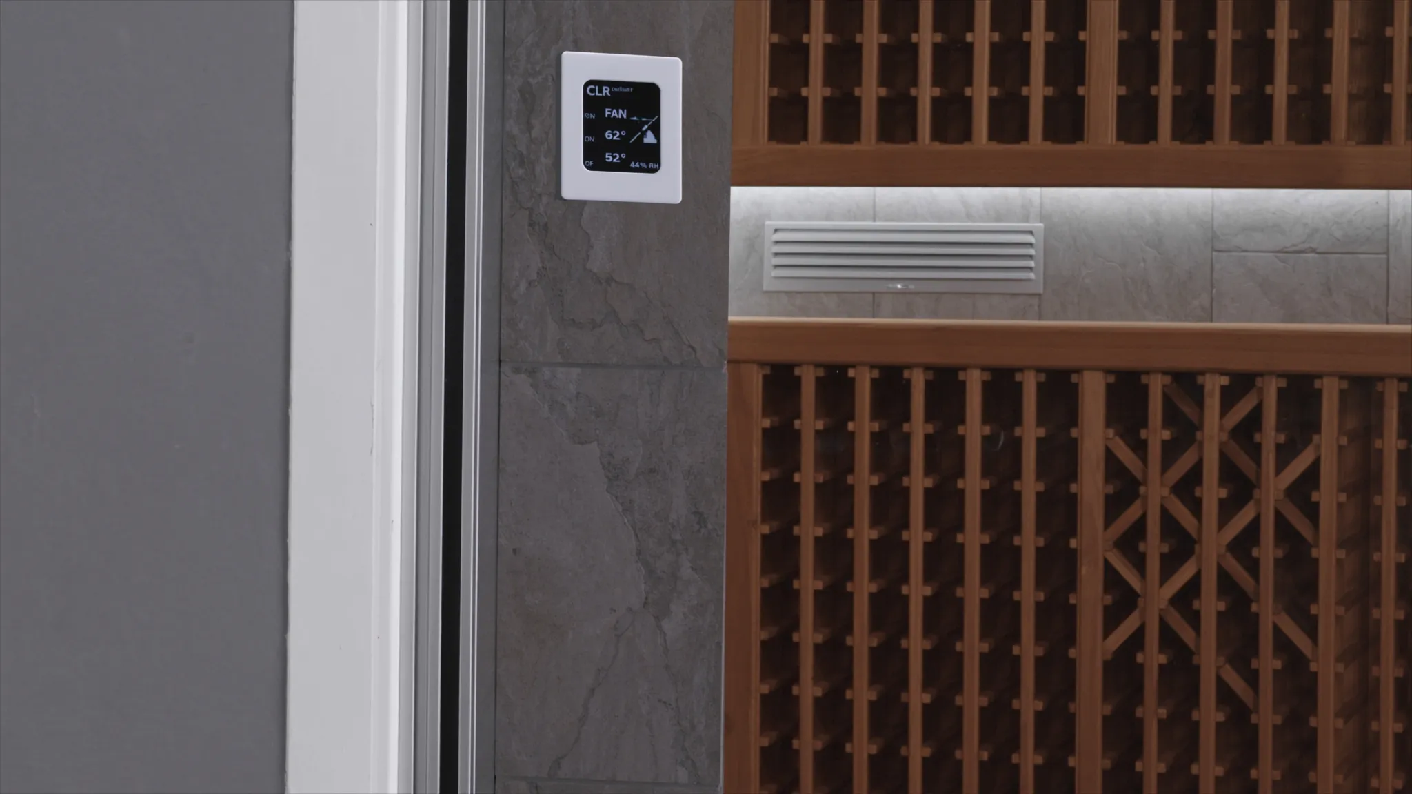 Wine cellar control panel and supply grille beside bottle racks, showing the building details behind a wine cellar refrigeration system